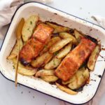 Top down image of Asian glazed salmon on a bed of crispy wedges in a baking tray with a serving spoon and tea towel