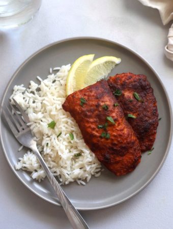 A dinner plate with rice and a tandoori fish portion.