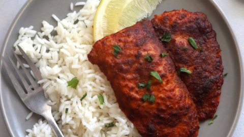 A dinner plate with rice and a tandoori fish portion.