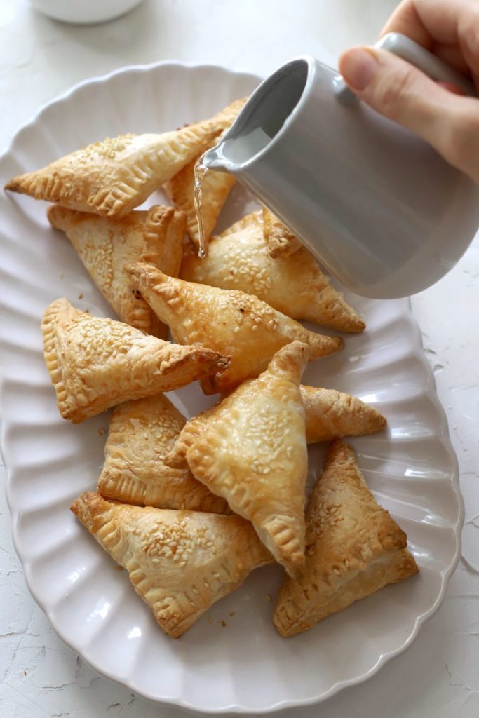 Simple syrup being poured on a platter of sweet Ramadan hand pies.