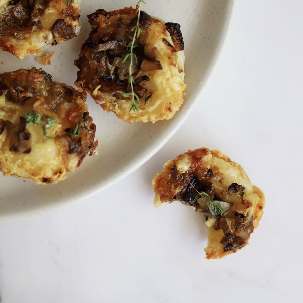 Close-up of a broken Camembert and mushroom tartlet with melted cheese and mushroom filling.