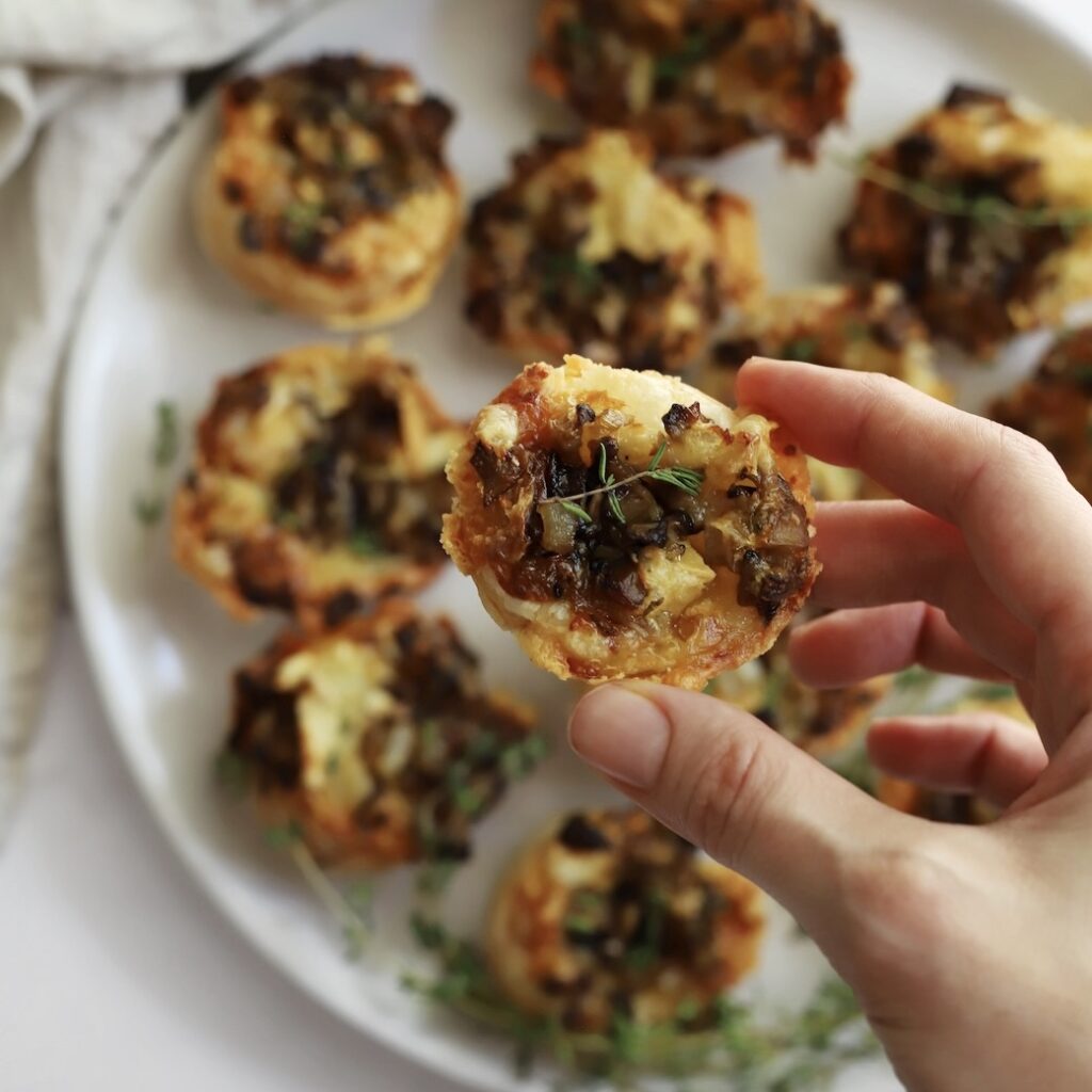 Camembert and mushroom tartlet held up to show the flaky pastry and mushroom filling.