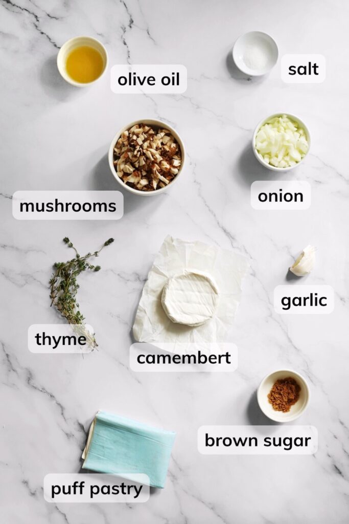 Ingredients for Camembert and mushroom tartlets, including puff pastry, mushrooms, Camembert, onion, garlic, thyme, and olive oil.