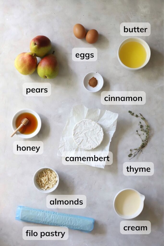 Ingredients for pear and Camembert tart, including filo pastry, pears, Camembert, cream, eggs, butter, cinnamon, and honey.