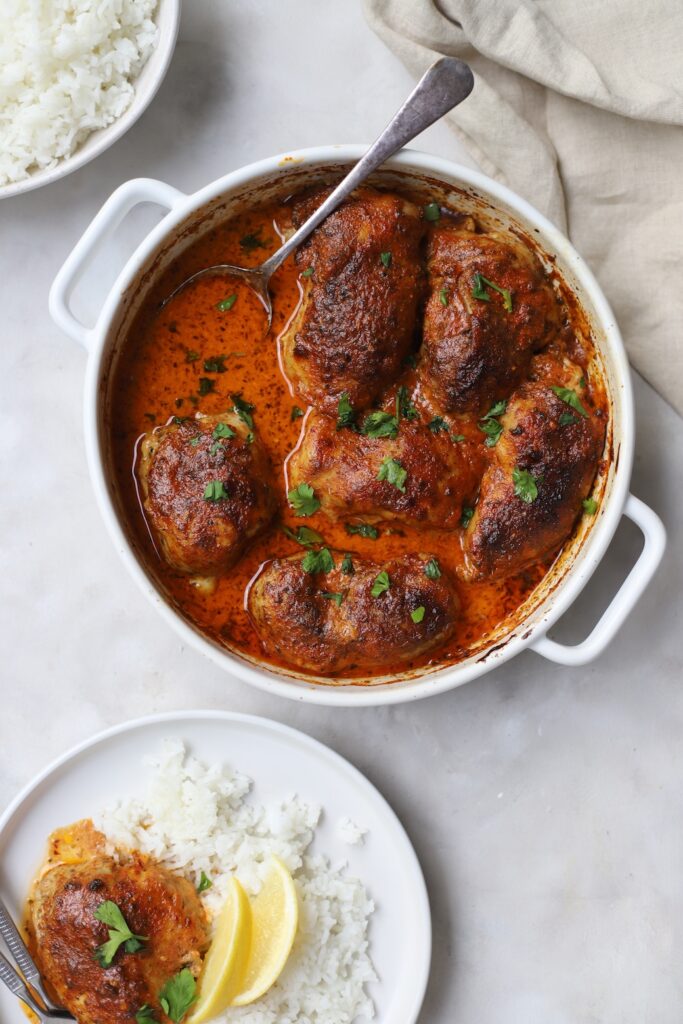 An overhead view of a weeknight Moroccan chicken dinner in a white ceramic roasting dish and served on a plate.
